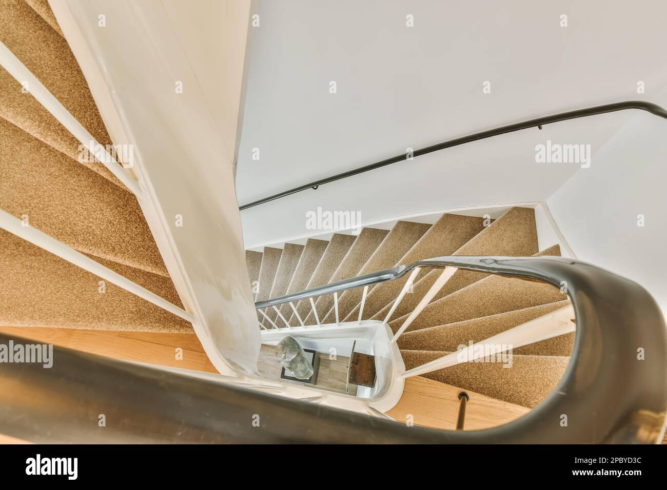 Dall'alto di una scala marrone a spirale con ringhiere metalliche in una casa luminosa con pareti bianche Foto Stock
