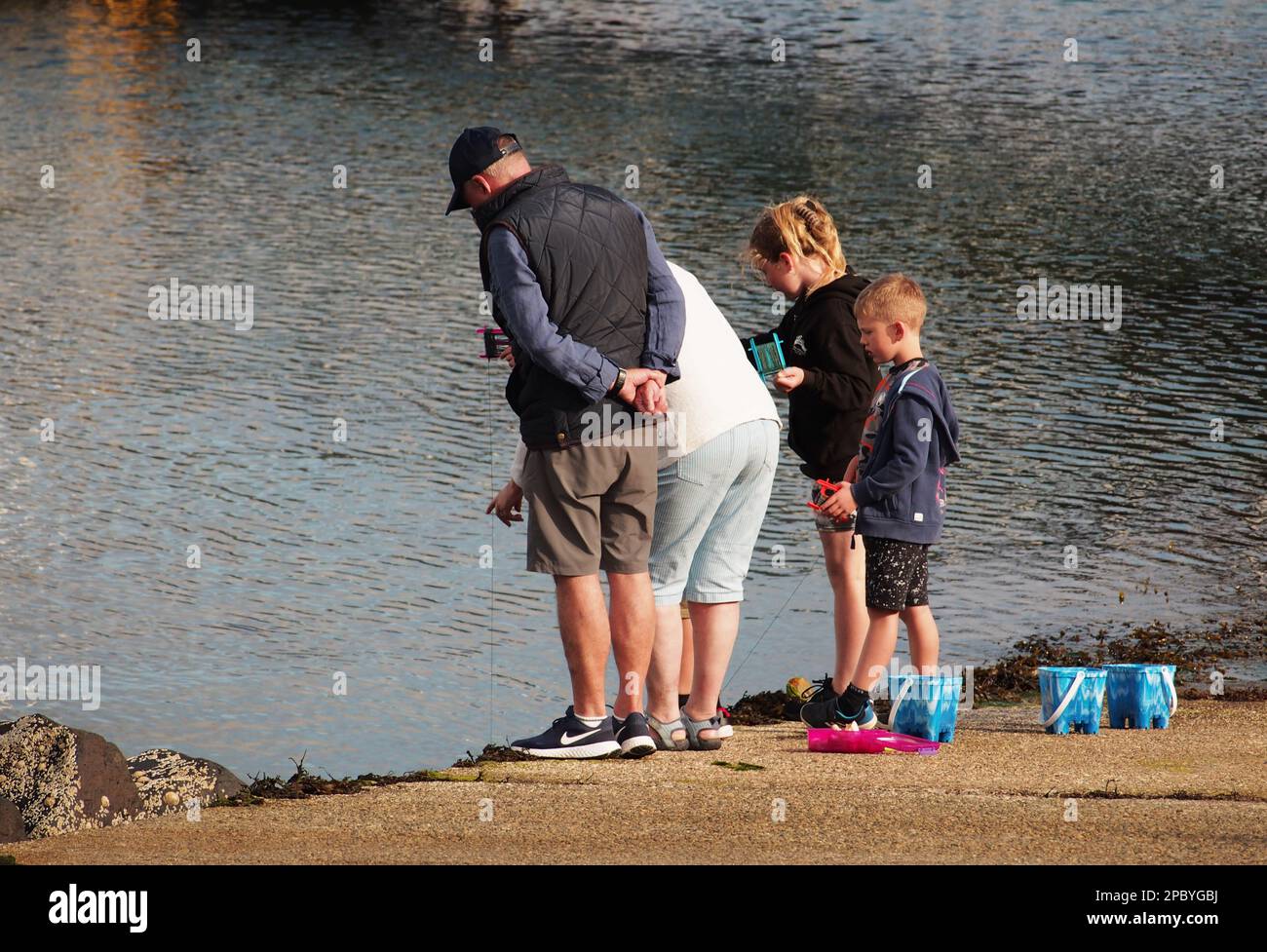 Due nonni si schiantano con i loro nipoti su una strada a Tobermory, Mull, Scozia. Regno Unito che mostra le loro linee di granchio e secchi colorati Foto Stock