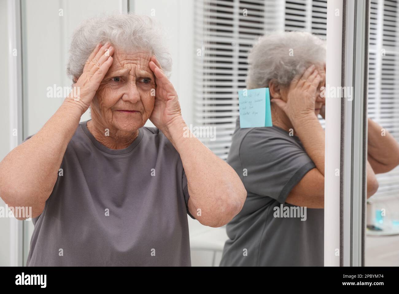 Donna anziana dimenticante vicino allo specchio con nota di promemoria all'interno. Compromissione della memoria correlata all'età Foto Stock