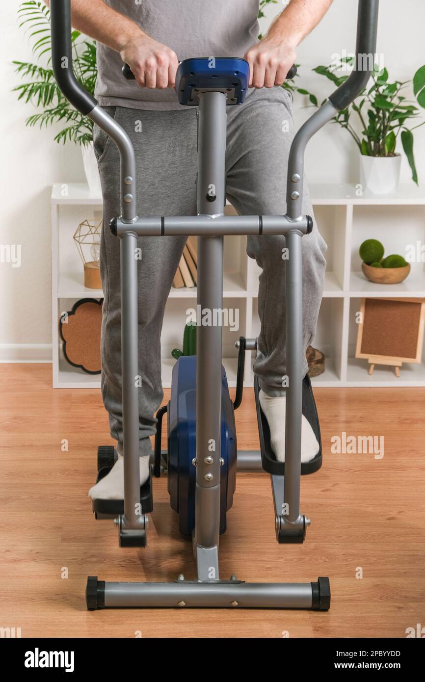 Un uomo si allena su una macchina ellittica. Allenatore sportivo a casa in appartamento. Sport a casa. Foto Stock
