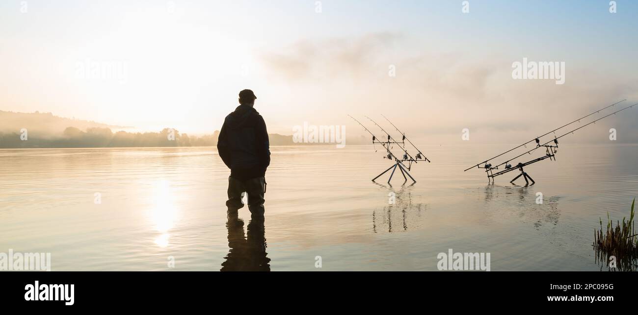 Avventure di pesca, pesca alla carpa. Pescatore con stivali sul lago al sorgere del sole in una mattina misty è la pesca con la tecnica di pesca al carpfishing Foto Stock