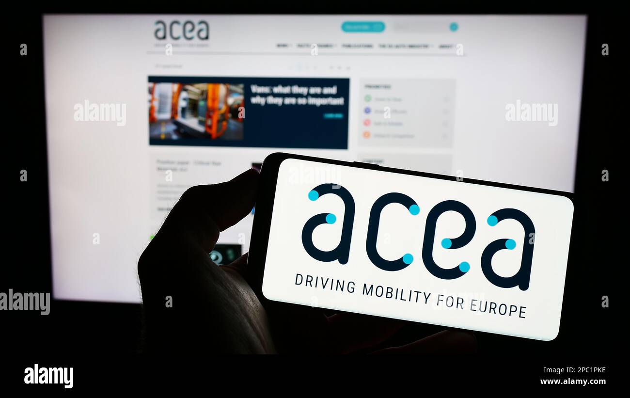 Persona che tiene il cellulare con il logo dell'Associazione europea dei costruttori di automobili (ACEA) sullo schermo di fronte alla pagina web. Messa a fuoco sul display del telefono. Foto Stock
