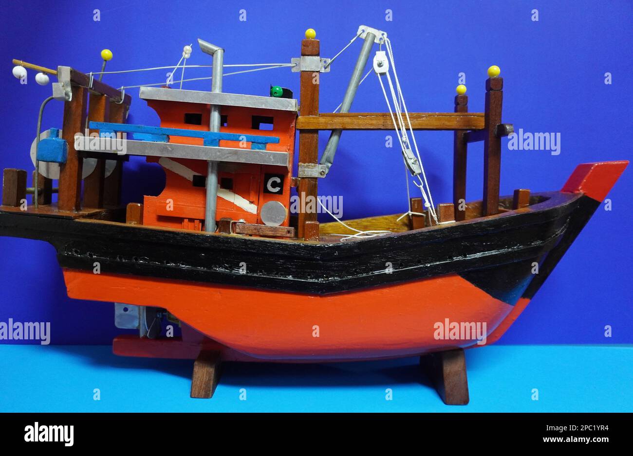 Una barca a vela giocattolo isolata in miniatura su uno sfondo blu brillante Foto Stock