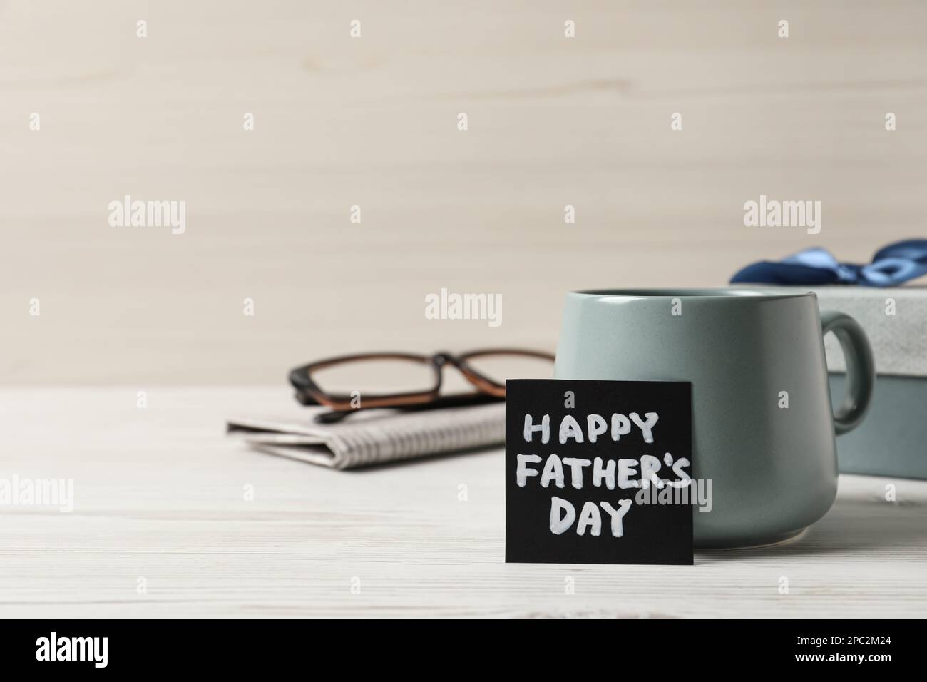 Carta con frase Festa del papà, tazza di caffè aromatico, confezione regalo e bicchieri su sfondo di legno bianco. Spazio per il testo Foto Stock