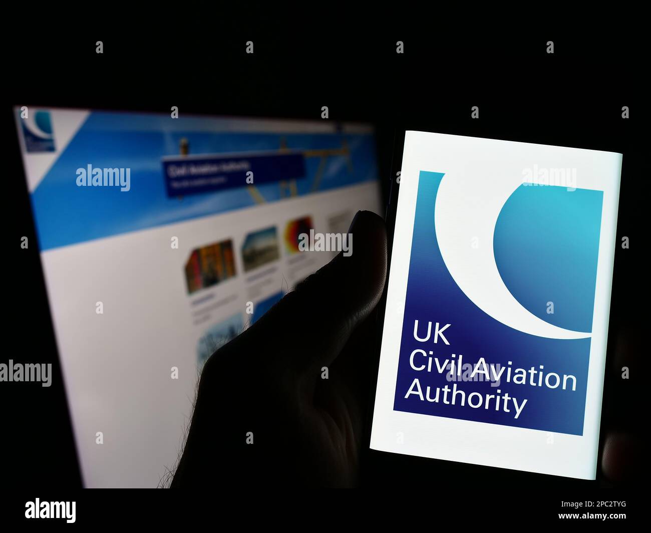 Persona che tiene in mano uno smartphone con il logo della British Regulator Civil Aviation Authority (CAA) sullo schermo di fronte al sito Web. Messa a fuoco sul display del telefono. Foto Stock