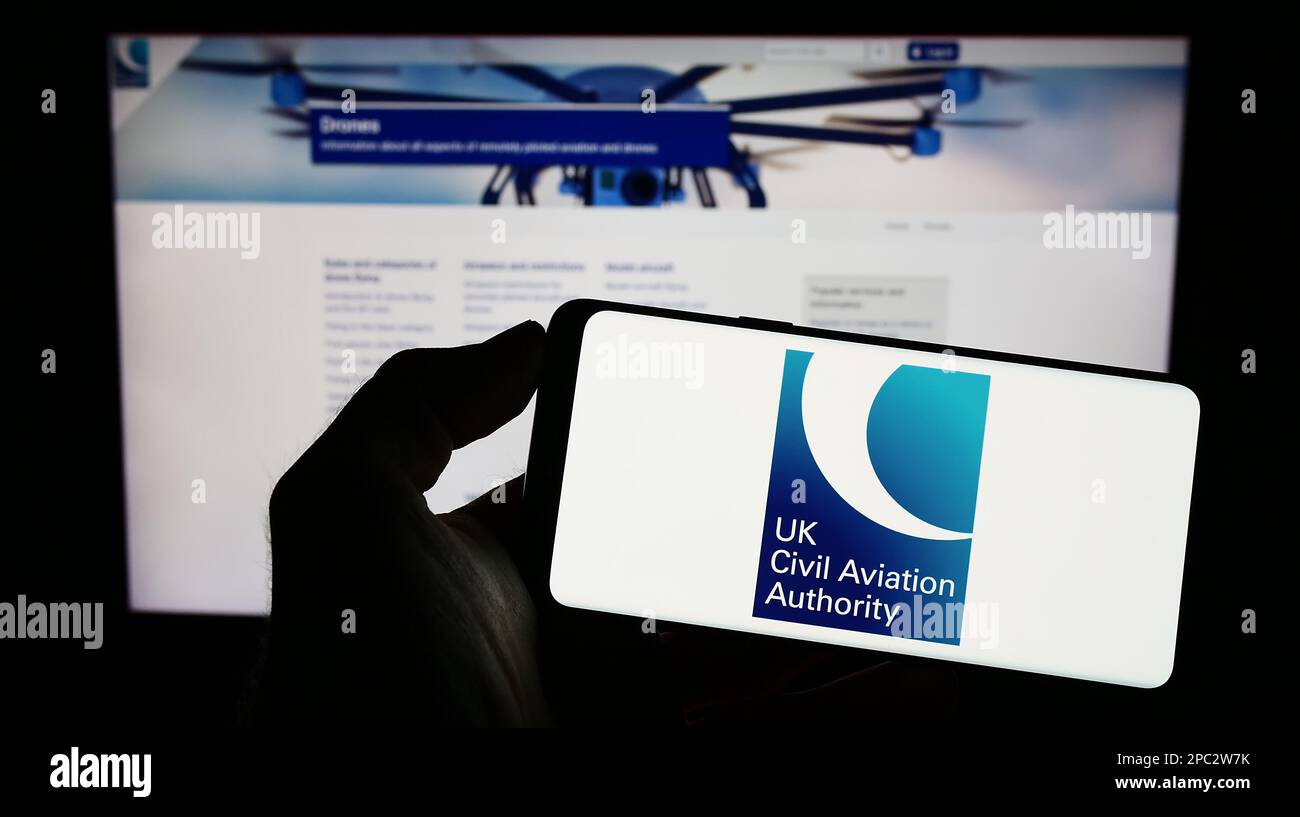 Persona che tiene il cellulare con il logo della British Regulator Civil Aviation Authority (CAA) sullo schermo di fronte alla pagina web. Messa a fuoco sul display del telefono. Foto Stock
