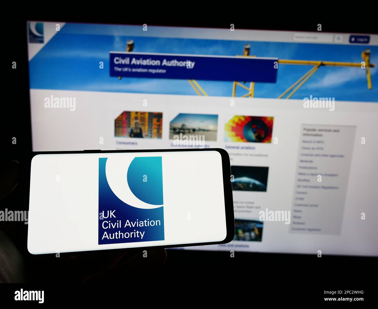 Persona che tiene il cellulare con il logo della British Regulator Civil Aviation Authority (CAA) sullo schermo di fronte alla pagina web. Messa a fuoco sul display del telefono. Foto Stock