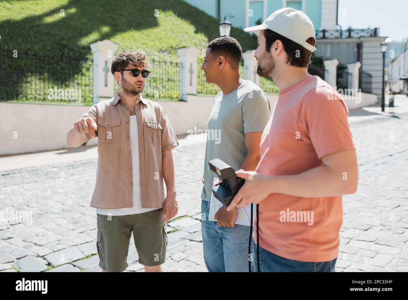 Giovane guida in occhiali da sole che parla vicino a turisti multietnici mentre conduce il tour nel quartiere di Podil a Kiev, immagine stock Foto Stock
