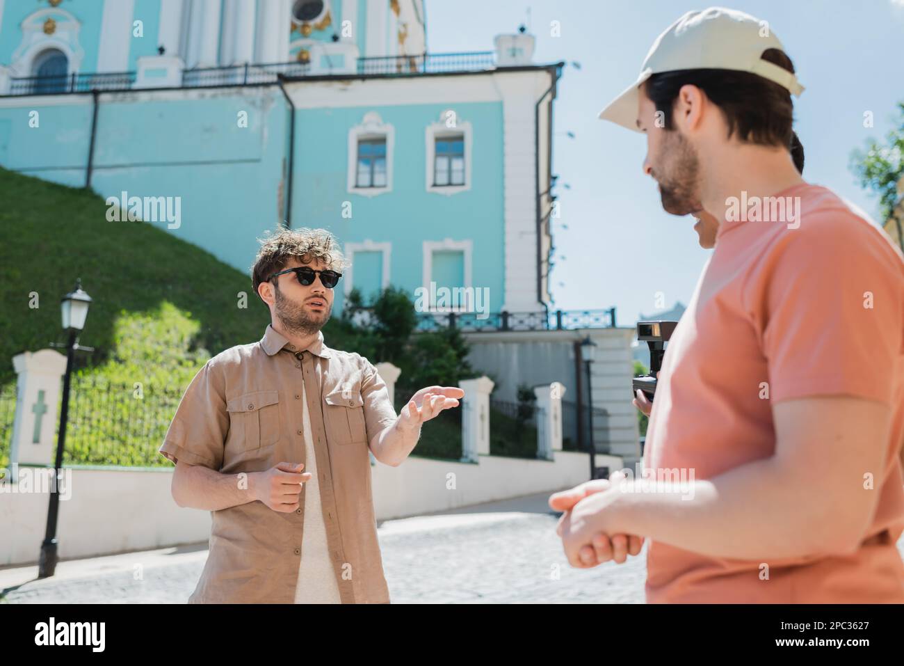 Giovane guida turistica in occhiali da sole che parla con i turisti multietnici sulla discesa di Andrews a Kiev, immagine stock Foto Stock
