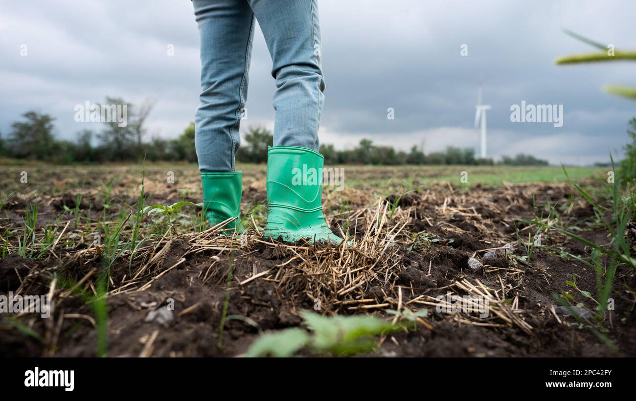 Primo piano stivali di contadino che lavora sul campo. Turbine eoliche all'orizzonte Foto Stock