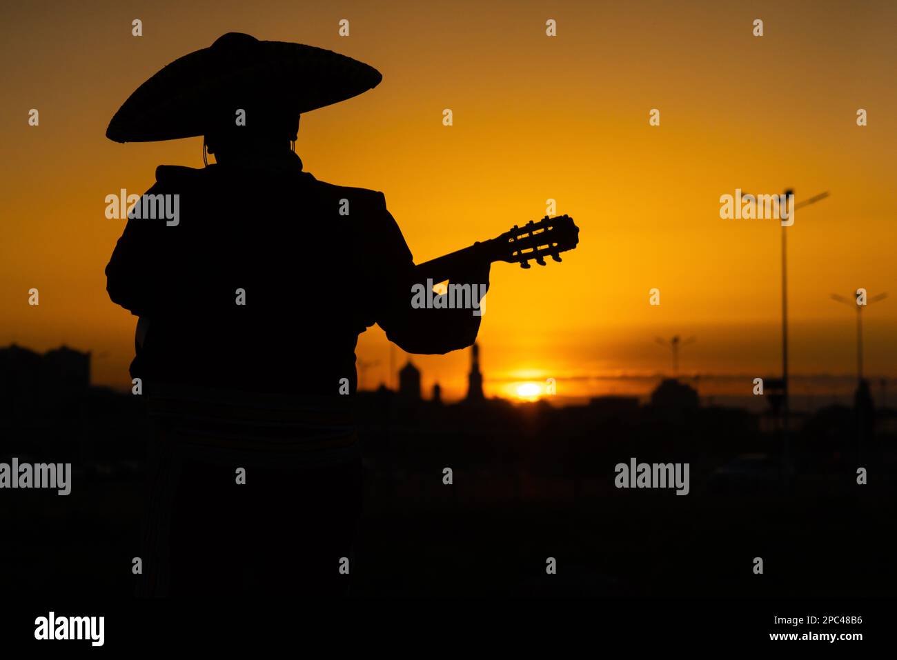 Silhouette di un musicista messicano mariachi con una chitarra sullo sfondo del panorama della città. Foto Stock