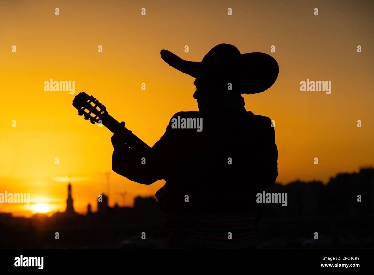 Silhouette di un musicista messicano mariachi con una chitarra sullo sfondo del panorama della città. Foto Stock