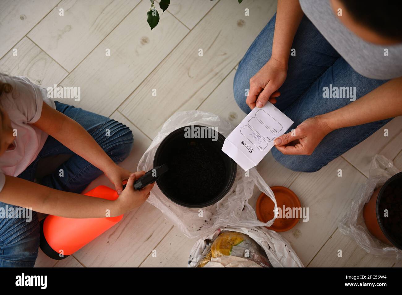 Vista dall'alto: Bambino annaffiare terreno in vaso con semi di piante, aiutando la sua mamma in hobby agricolo. Amate e salvate il pianeta Foto Stock