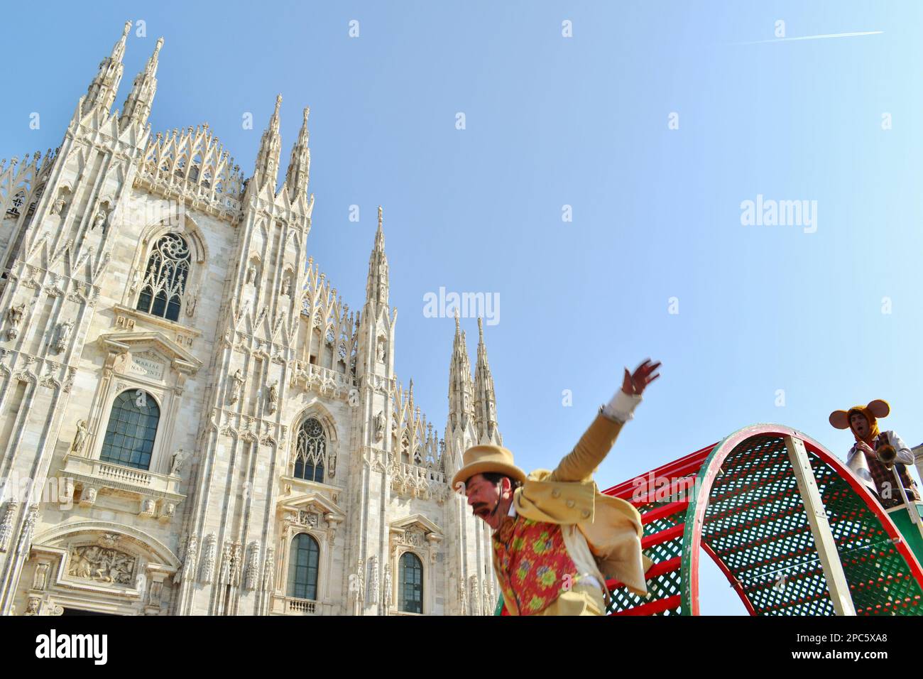 L'esecutore del circo vestito in una maschera di carnevale del cilindro del cappello sta cadendo giù la ruota del criceto. Sullo sfondo il Duomo di Milano. Foto Stock