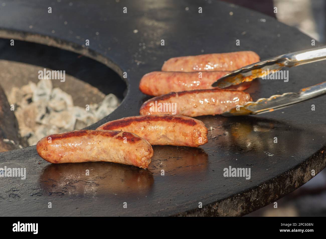 Salsicce di maiale pronte da mangiare, grigliate o arrostite in un barbecue su un fuoco aperto e fiamme, in un mercato di cibo di strada o un picnic all'aperto, primo piano Foto Stock