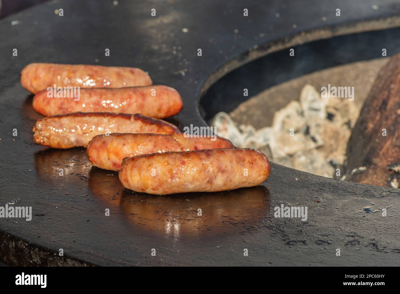 Salsicce di maiale pronte da mangiare, grigliate o arrostite in un barbecue su un fuoco aperto e fiamme, in un mercato di cibo di strada o un picnic all'aperto, primo piano Foto Stock