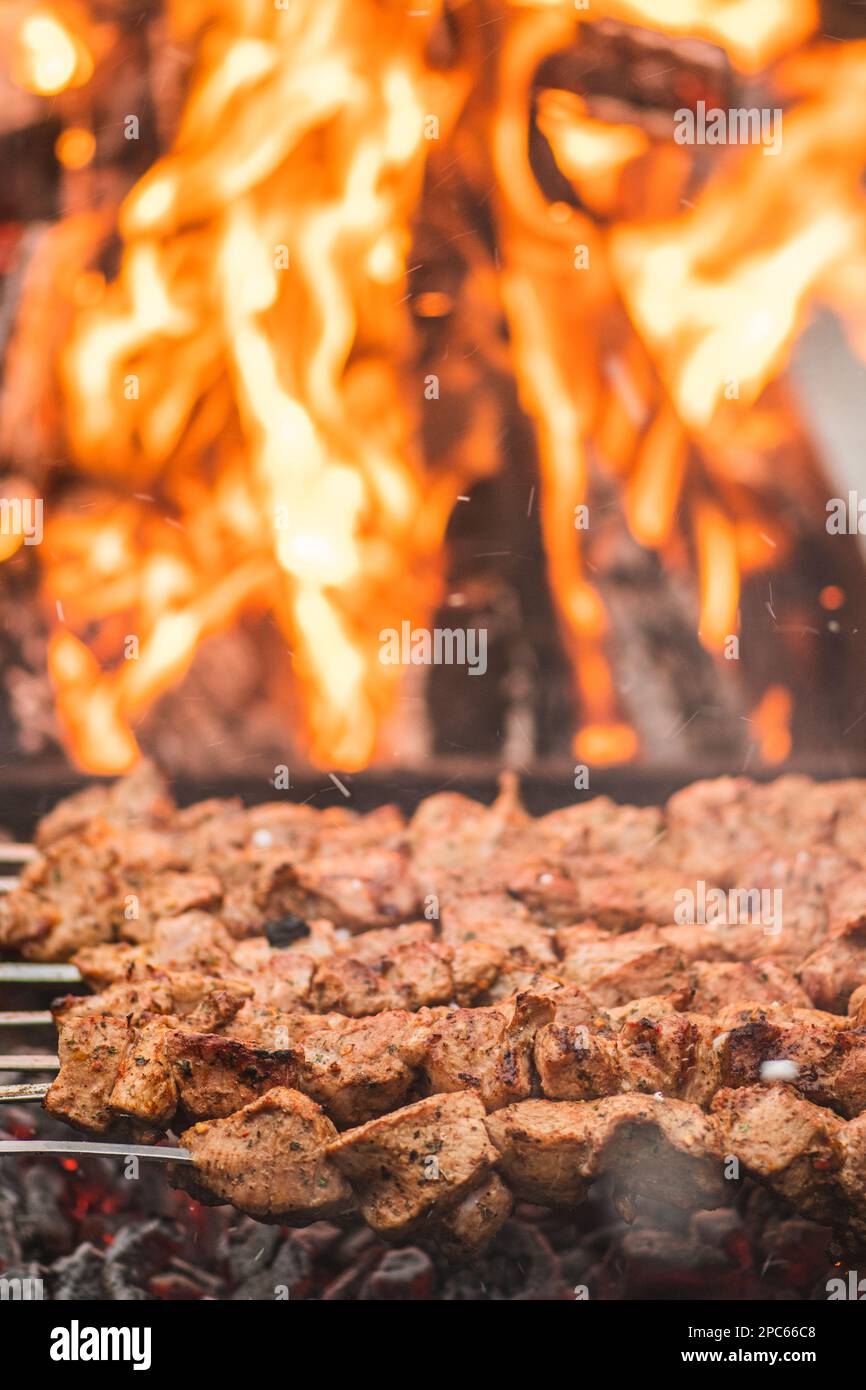 Spiedino di carne di maiale, grigliato o arrostito in un barbecue con forchette a fuoco aperto e fiamme, shashlik o shashlik in un mercato di cibo di strada, verticale Foto Stock