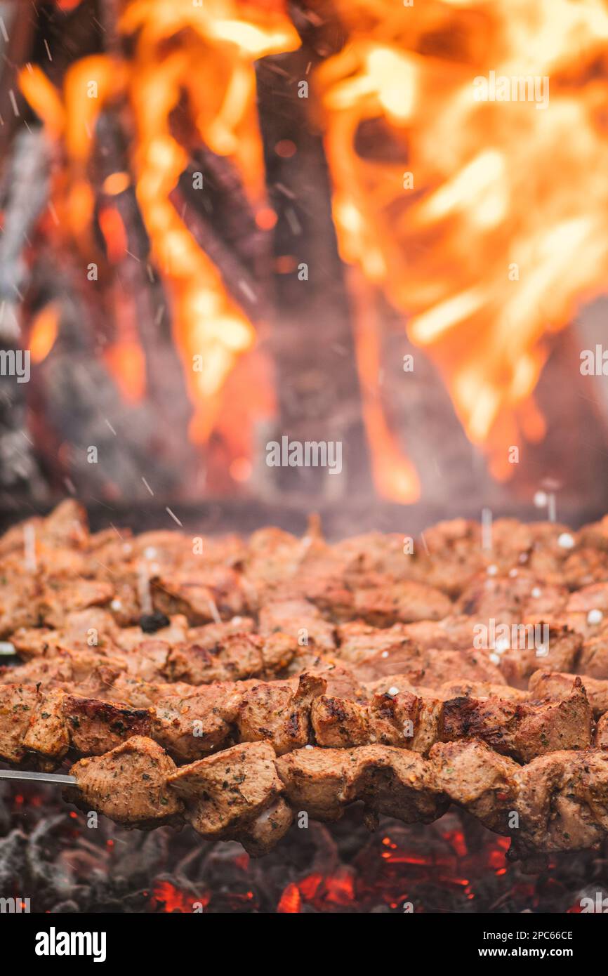 Spiedino di carne di maiale, grigliato o arrostito in un barbecue con forchette a fuoco aperto e fiamme, shashlik o shashlik in un mercato di cibo di strada, verticale Foto Stock