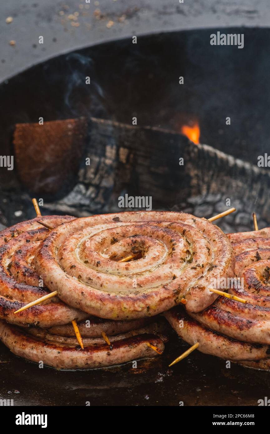 Salsicce arrotolate a spirale preparate con carne macinata alla griglia o arrostite in un barbecue sul fuoco aperto, verticale Foto Stock