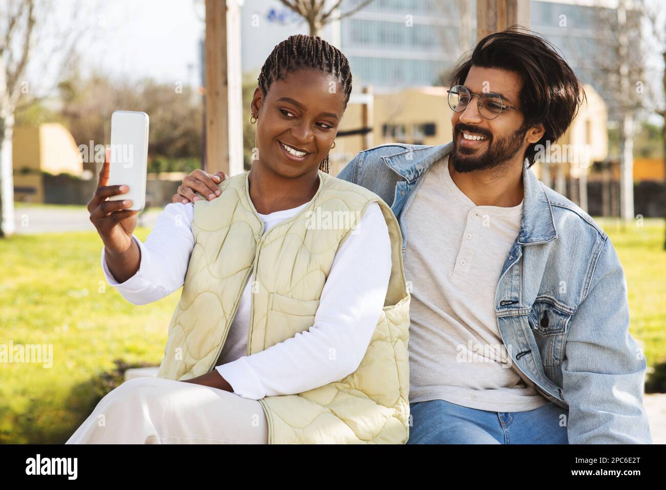 Allegro giovane nero, arabo persone studenti studiare con smartphone insieme, hanno riunione all'aperto, fare selfie Foto Stock