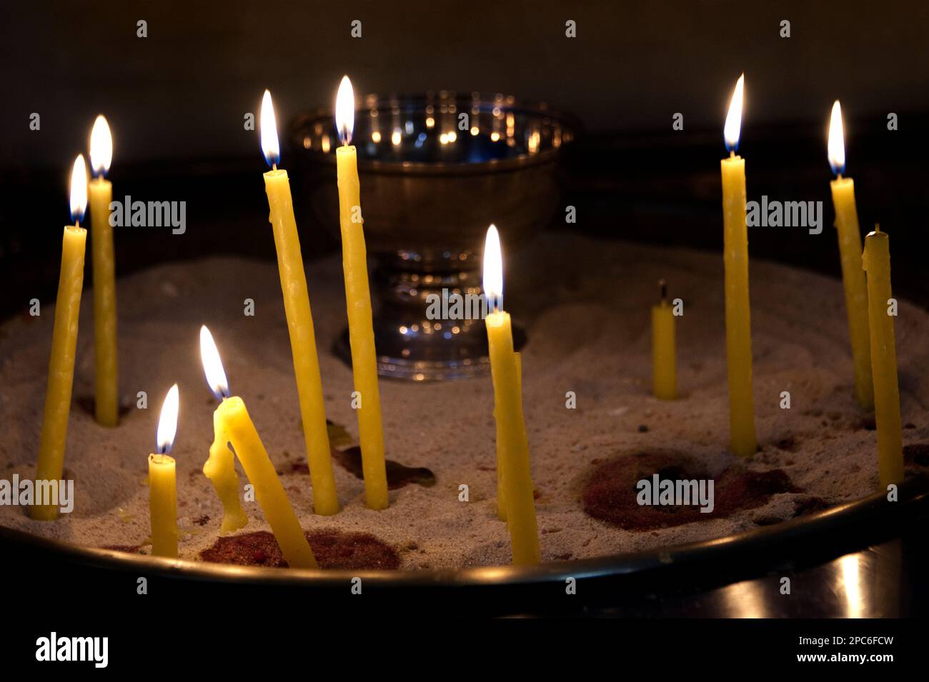 Molte candele gialle che bruciano in una chiesa come simbolo di credenza e speranza Foto Stock