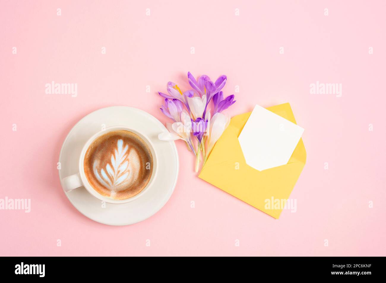 Tazza da caffè, bouquet di fiori primaverili e busta con scheda vuota. Vista dall'alto, piatto, mockup. Foto Stock