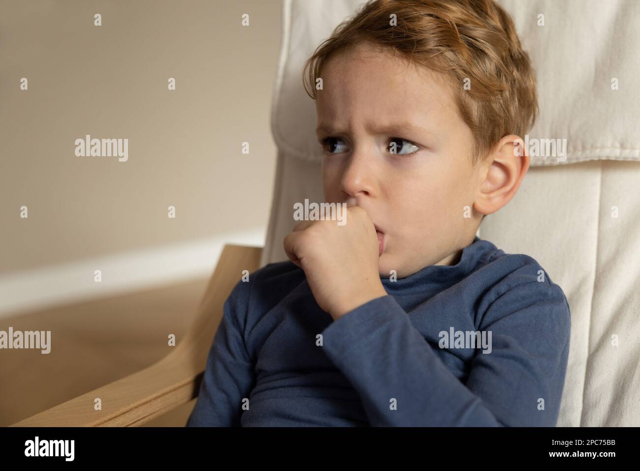 Un ragazzino si siede con un volto teso e succhia il pollice della mano sinistra. Foto Stock