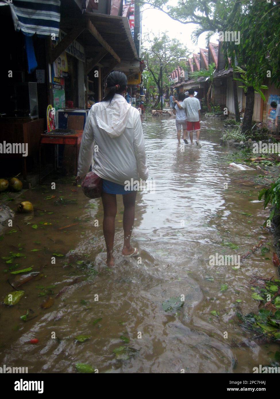 Tourists wade through a flooded street along shopping stalls at the popular tourist island of Boracay in Kalibo, Aklan province, central Philippines, Sunday, Dec. 10, 2006. Typhoon Utor lashed the central and eastern Philippines Sunday, killing four people, including three children. The typhoon's path was just south of the eastern Bicol region, where more than 1,000 people were killed or left missing after Typhoon Durian struck last week. (AP Photo/Andree Abriam) Foto Stock