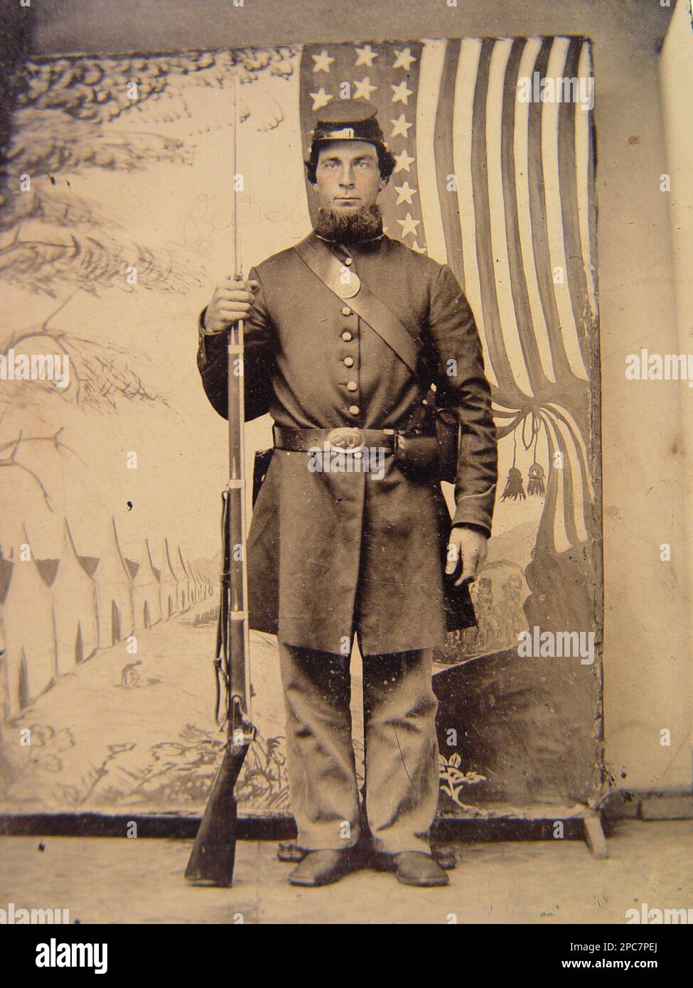 Soldato non identificato in uniforme Union e cappello da foraggio con muschio bayoneted di fronte allo sfondo dipinto che mostra campo militare e bandiera americana. Stati Uniti, Esercito, persone, 1860-1870, soldati, Unione, 1860-1870, uniformi militari, Unione, 1860-1870, Fucili, 1860-1870, Bayonets, 1860-1870, sfondi, 1860-1870, Stati Uniti, Storia, Guerra civile, 1861-1865, Personale militare, Unione. Foto Stock