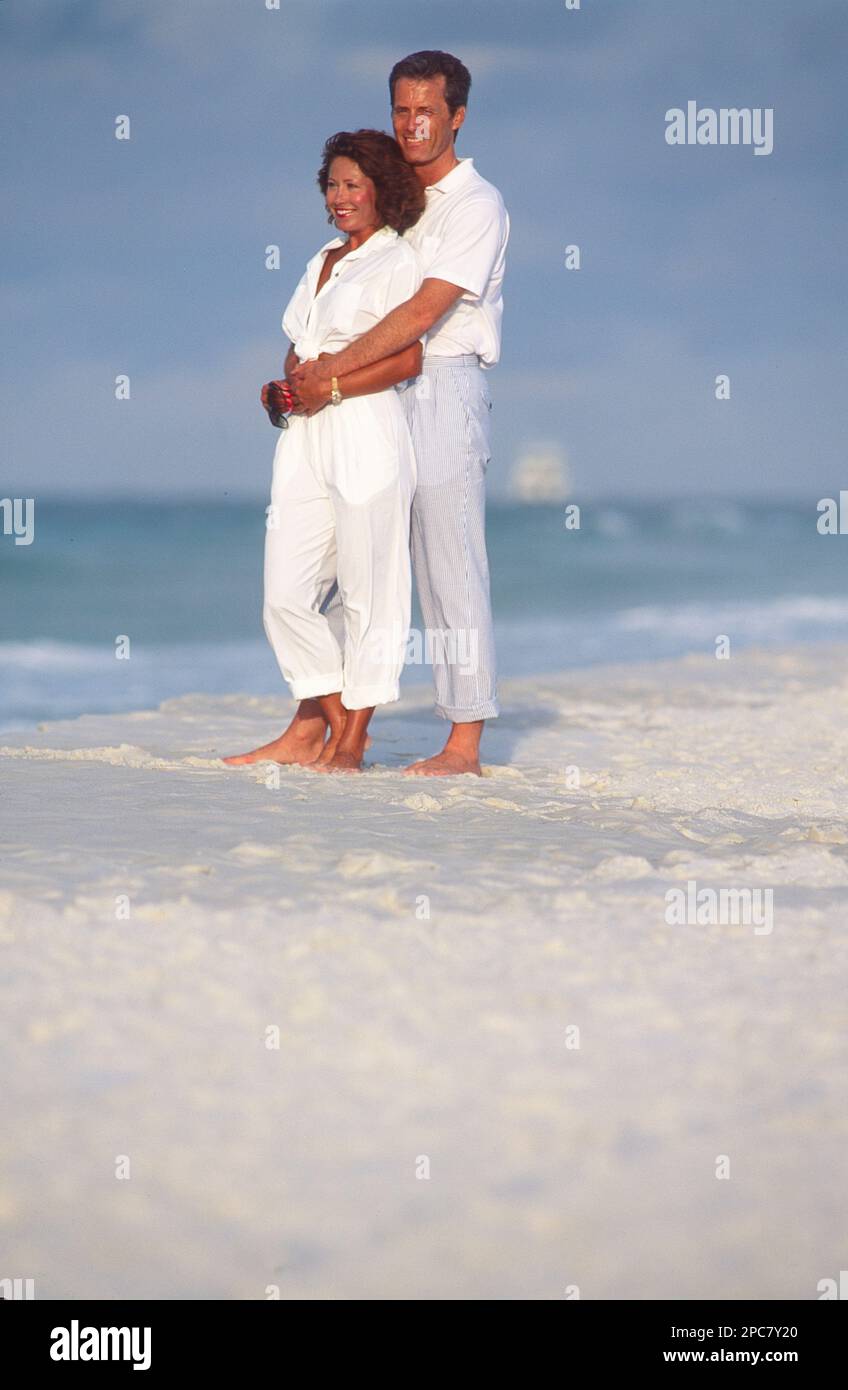 Giovane coppia in piedi nella sabbia alla spiaggia, ma l'oceano come sfondo, l'uomo ha le braccia intorno alla donna come hanno guardato fuori Foto Stock