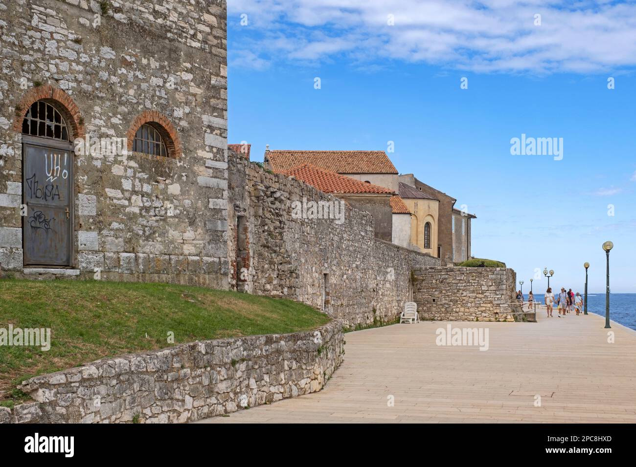 I turisti che camminano sul lungomare lungo le antiche mura della città di Poreč / Parenzo, località balneare sul mare Adriatico, Istria County, Croazia Foto Stock