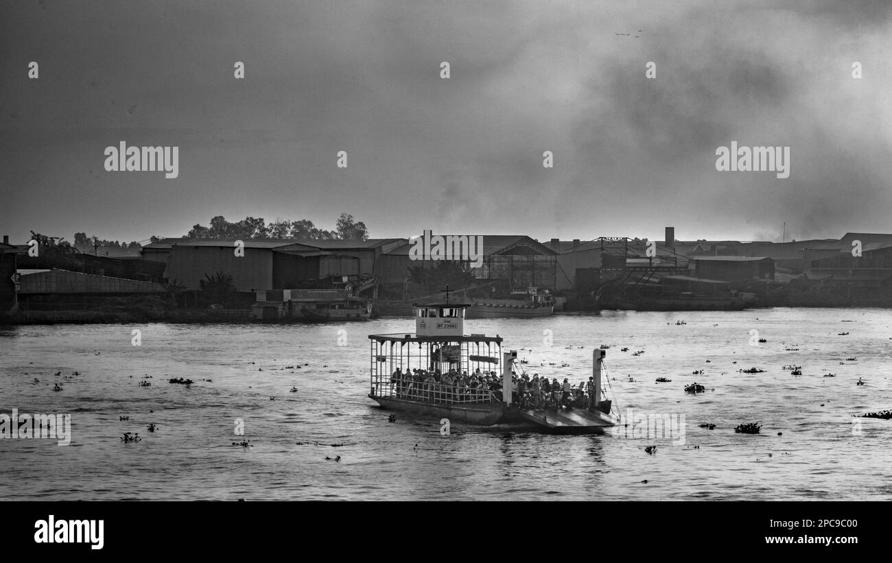 Un traghetto attraversa il fiume Mekong all'alba vicino a Long Xuyen nel delta del Mekong in Vietnam, mentre il fumo sale da forni di mattoni vicino alla riva del fiume. Foto Stock
