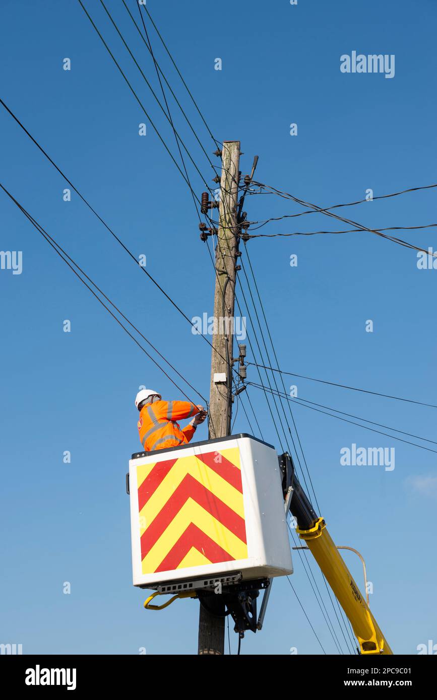 Ingegnere delle telecomunicazioni che lavora su fili su un palo telegrafico. Riparazioni telefoniche o a banda larga in corso ad un'altezza dalla piattaforma di sollevamento Foto Stock