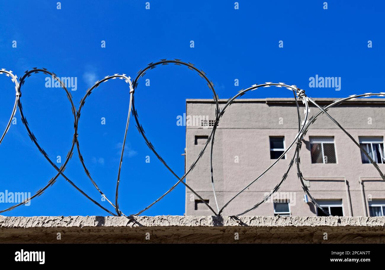 Filo spinato sulla parte superiore del muro e buikding grigio sullo sfondo Foto Stock