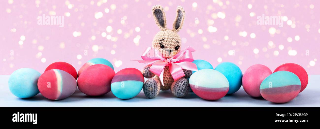 Uova di Pasqua dipinte in cremisi e blu con coniglietto di pasqua accovacciato su sfondo rosa con luci magiche. Buon concetto di Pasqua. Banner Foto Stock