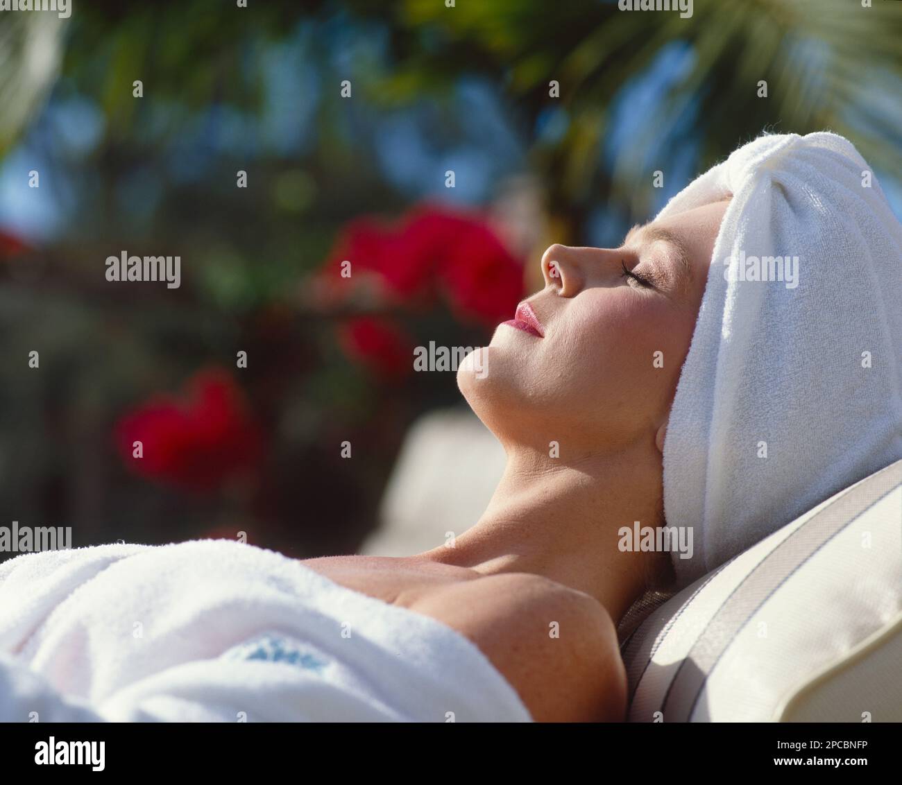 Donna in un accappatoio bianco e un asciugamano capo avvolgente sdraiata su una chaise longue che si prendisole Foto Stock