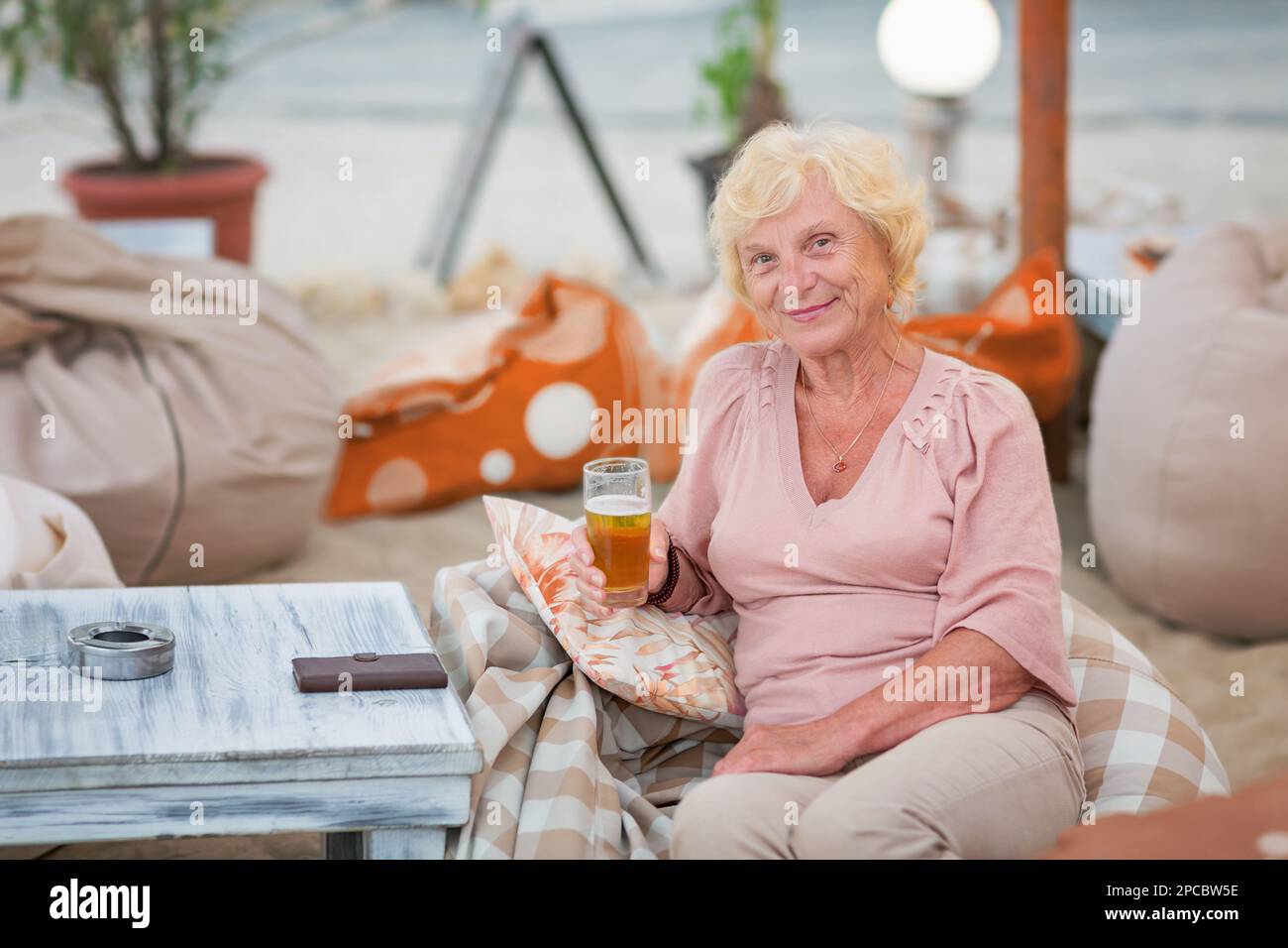 Donna matura seduta a un tavolo in un bar estivo e bere birra Foto Stock
