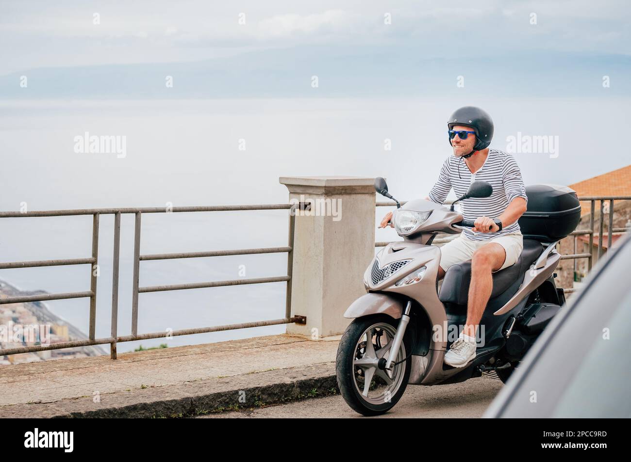 Uomo allegro e sorridente in casco e occhiali da sole che guida veloce il  moto scooter sulle strade della città vecchia siciliana nella forza d'Agro.  Felice vacanza italiana Foto stock - Alamy