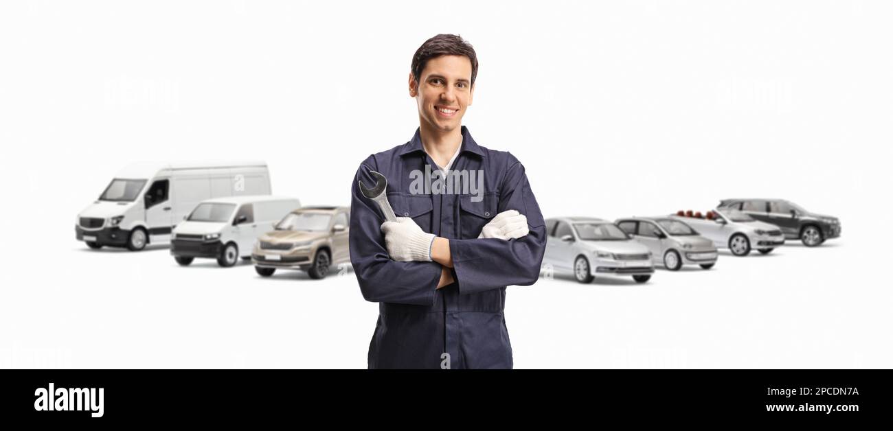 Giovane meccanico in uniforme che tiene una chiave con i veicoli nella parte posteriore isolati su sfondo bianco Foto Stock