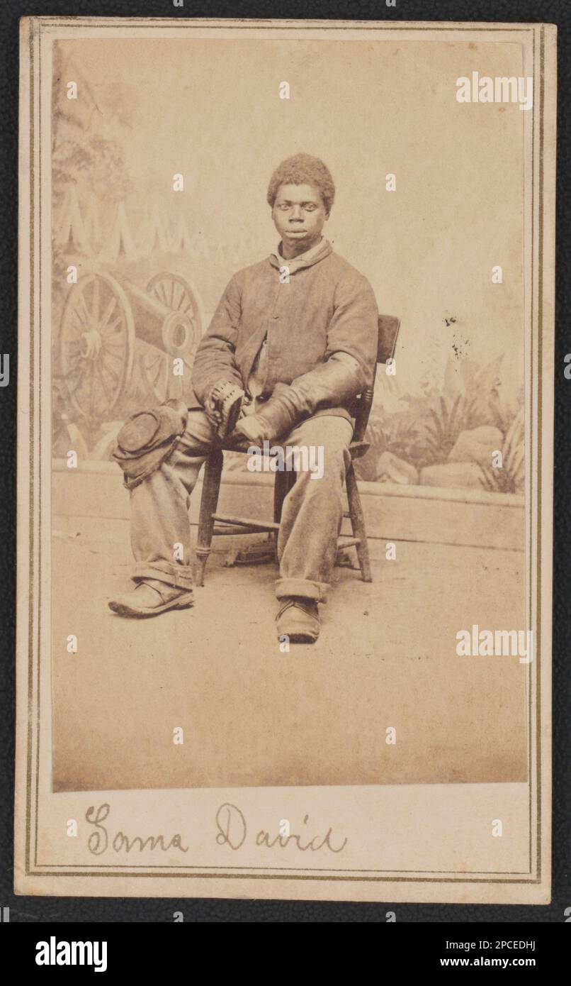 Soldato afro-americano non identificato in uniforme Union di fronte allo sfondo dipinto che mostra cannone e campo militare, lucidando uno stivale. Liljenquist Famiglia Collezione di fotografie della Guerra civile , pp/liljpaper. Stati Uniti, esercito, persone, 1860-1870, afroamericani, Servizio militare, 1860-1870, soldati, Unione, 1860-1870, Uniformi militari, Unione, 1860-1870, backdrops, 1860-1870, Shoe Shining, 1860-1870, Stati Uniti, Storia, Guerra civile, 1861-1865, personale militare, Unione. Foto Stock