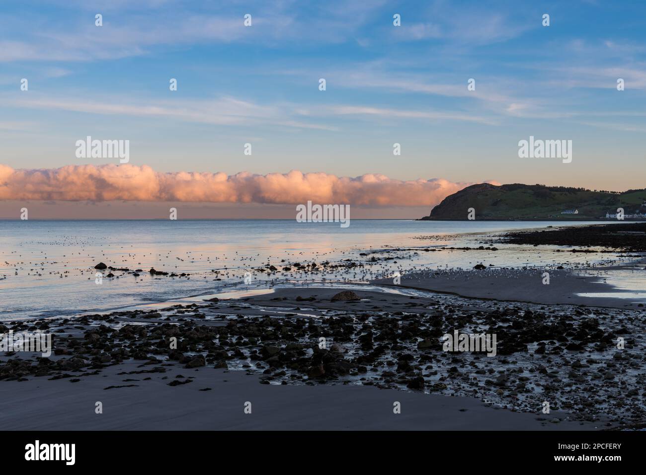 Una linea di nuvole colorate attraverso l'orizzonte al tramonto sopra la spiaggia e la costa della costa di Antrim, Irlanda del Nord Foto Stock