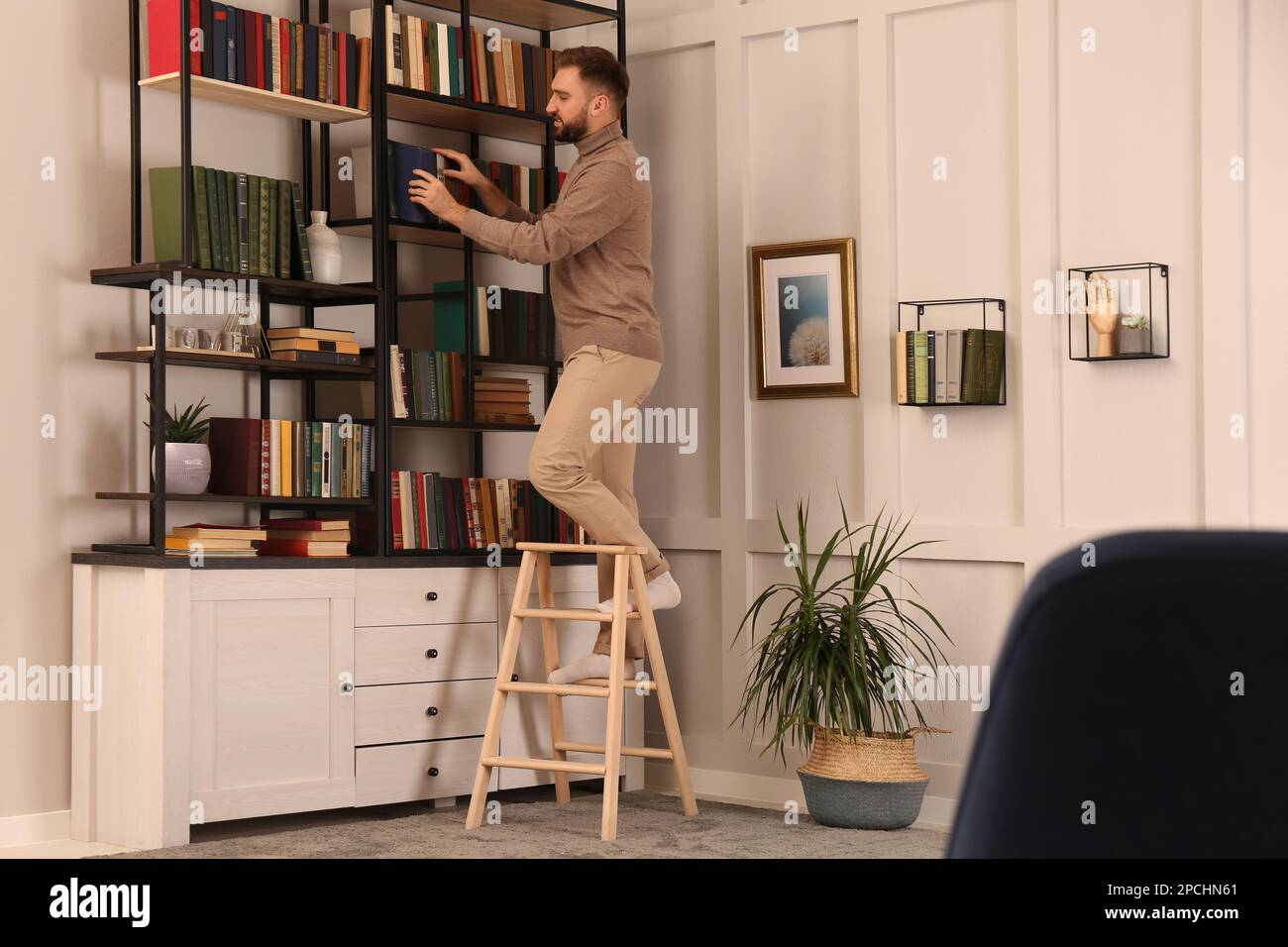 Libro di scelta del giovane uomo sulla mensola nella biblioteca domestica Foto Stock