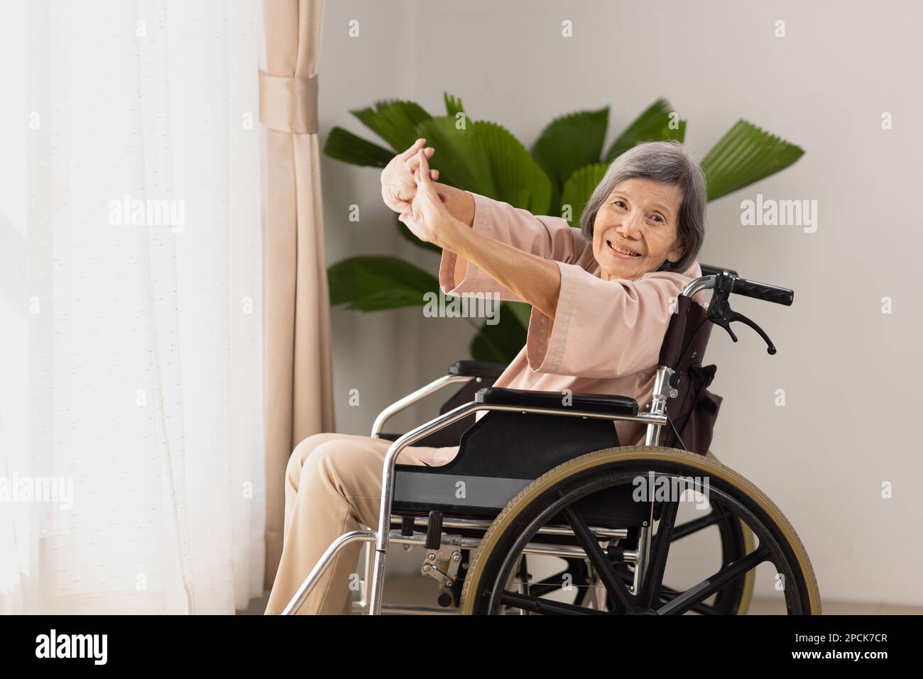 donna asiatica anziana che fa esercizi di stretching su sedia a rotelle nel soggiorno di casa Foto Stock