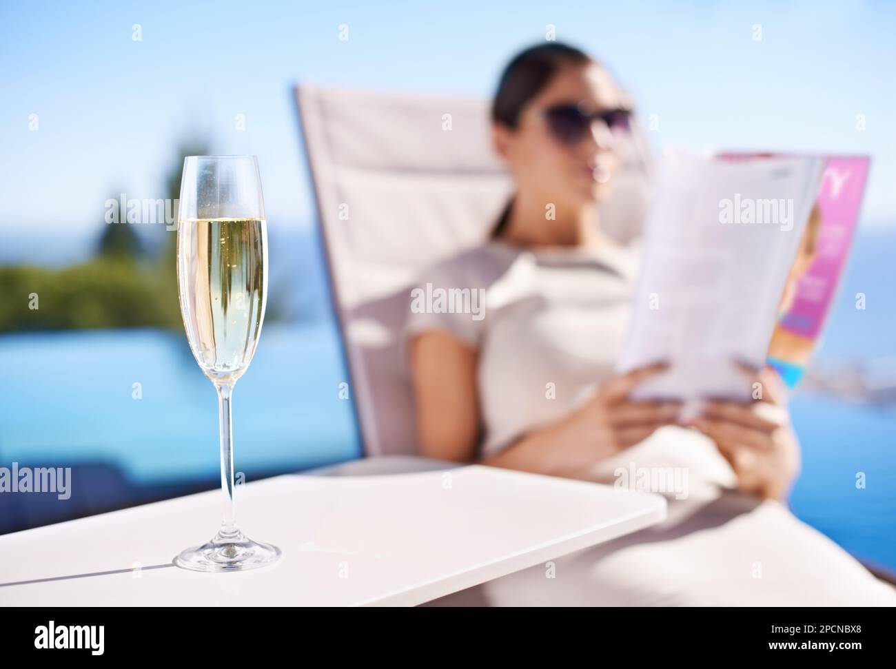 Non è questa la vita... una donna ben vestita sdraiata su una sedia a sdraio a bordo piscina e che legge un giornale. Foto Stock