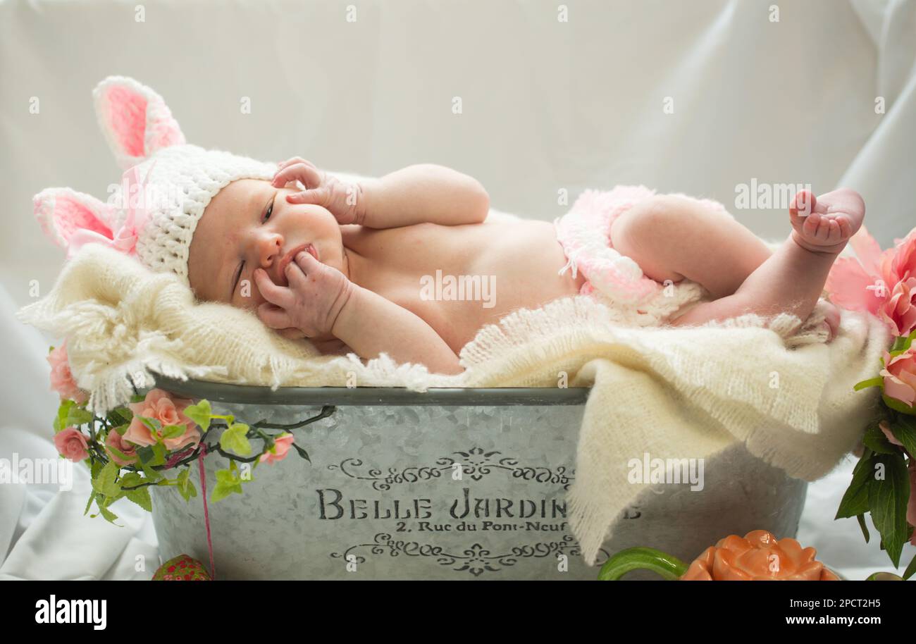 Primo piano di una bella bambina neonato che indossa un costume da coniglietto di pasqua bianco e rosa in un giardino fiorito prop . Foto Stock