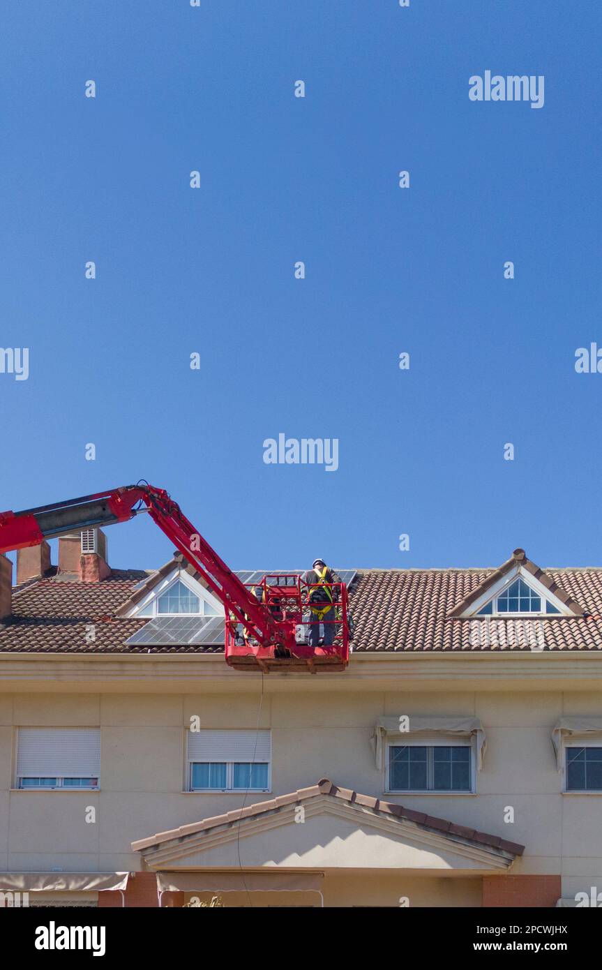 Operai che installano pannelli solari sul tetto di una casa a schiera. Lavorano sul sollevatore del braccio articolato Foto Stock