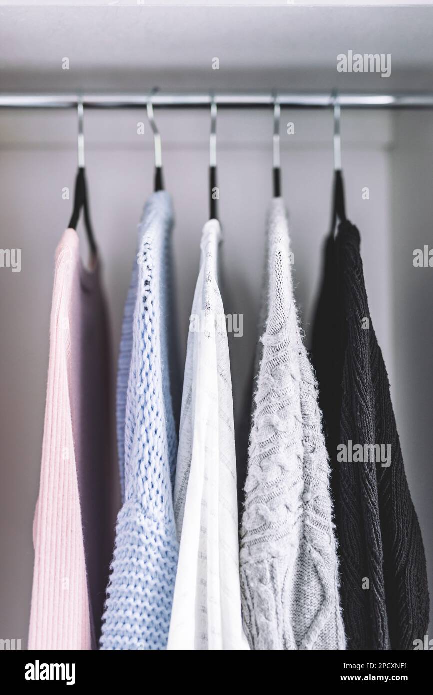 selezione minimalista di maglioni da donna e cardigan appesi all'asta del guardaroba con appendiabiti coordinati sparati a profondità di campo ridotta Foto Stock