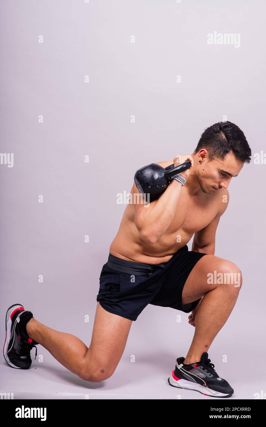 Atleta maschile ispanico allenarsi con kettlebell su sfondo grigio. Tema di allenamento CrossFit. Foto Stock