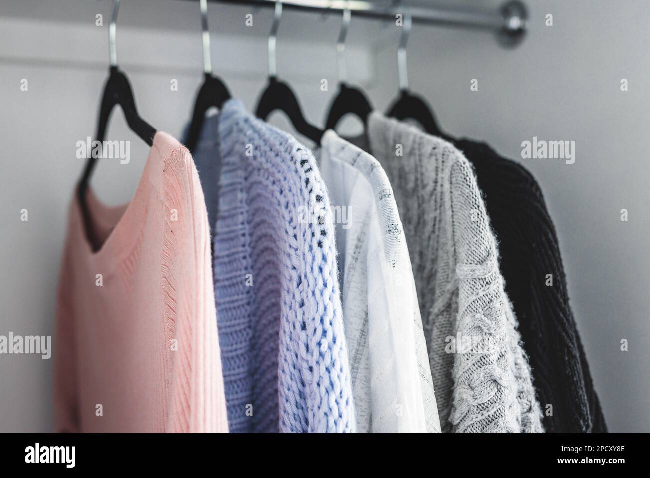 selezione minimalista di maglioni da donna e cardigan appesi all'asta del guardaroba con appendiabiti coordinati sparati a profondità di campo ridotta Foto Stock
