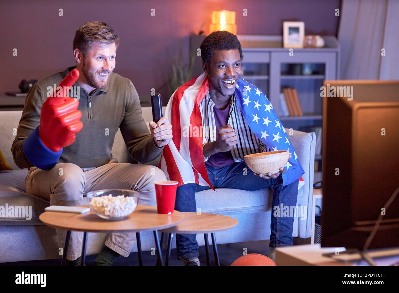 Ritratto completo di due appassionati di sport che guardano la TV in luce blu e indossano la bandiera degli Stati Uniti Foto Stock